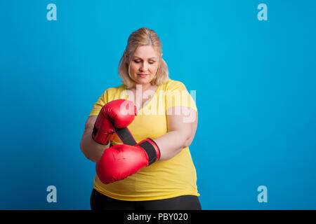 Portrait of a happy overweight woman putting on boxing gloves in studio.