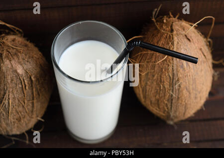 A glass of coconut milk and two whole coconuts on wooden background. Stock Photo
