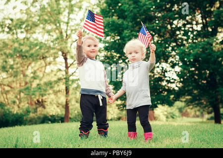 Happy adorable little blond Caucasian girl and boy smiling laughing holding hands and waving American flag outside  celebrating 4th july,  Independenc Stock Photo