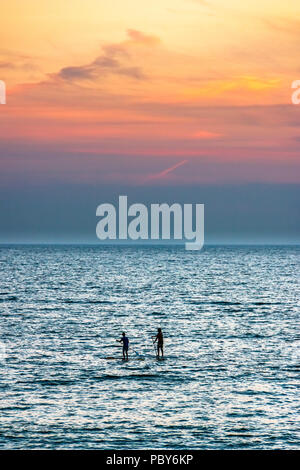 Two paddleboarders silhouetted against the sunset at Westward Ho!, Devon, UK Stock Photo