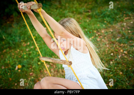A child cute girl swinging on a rope ladder in summer in the garden Stock Photo