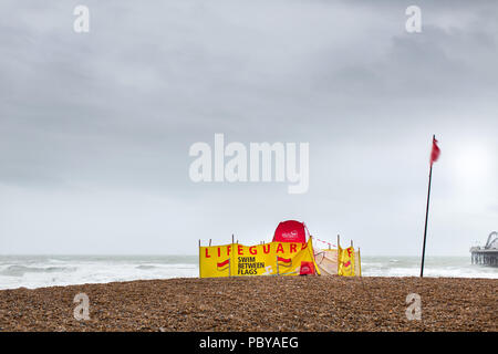 View of a lifeguard base on Brighton Beach. The red flag is flying and warning people to swim between flags but it is too rough to swim in the sea. Stock Photo