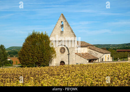 The picturesque little church in the hamlet of Lieu dit Saint Leger near Tournon d'Agenais is seen beyond a field of ripening sunflowers in rural   Lot et Garonne countryside, France Stock Photo