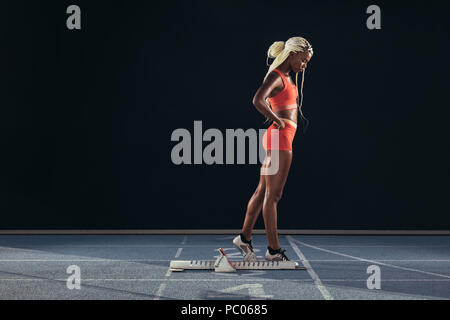 Female sprinter standing beside a starting block on running track on a ...