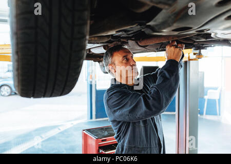 Car mechanic working on a lifted automobile at service station. Experienced repair man working in his garage. Stock Photo