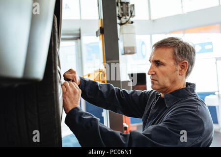 Side view of mechanic fastening the tyre on a vehicle lifted on ramp. Man replacing wheel of a car in garage. Stock Photo