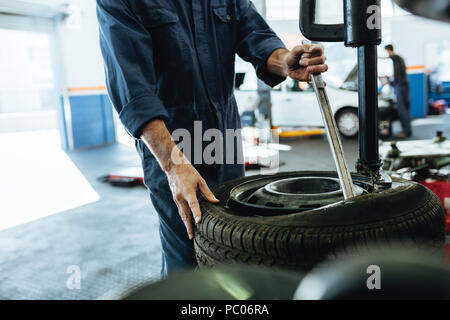 Mechanic changing car tire on a tire changing machine in workshop. Cropped shot of mechanic hands removing tire from disc on machine. Stock Photo