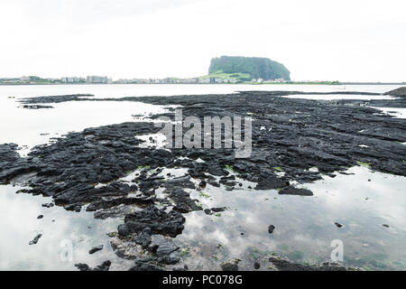 Black lava formation from lake view to green Ilchulbong volcano crater, Seongsan, Jeju Island, South Korea Stock Photo