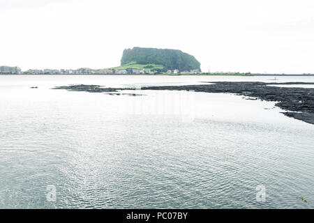 Black lava formation from white lake view to green Ilchulbong volcano crater, Seongsan, Jeju Island, South Korea Stock Photo