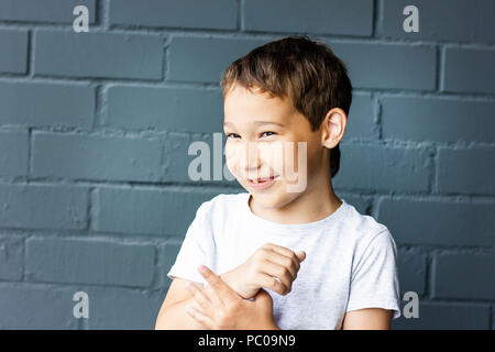 Cute 8 years old smiling boy confused on grey brick wall background Stock Photo