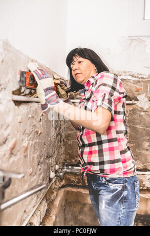 Clever woman repairing her bathroom sink pipe with  positive attitude. Woman using  Bubble Spirit Water Ruler Tool  and checking the tubes in the bath Stock Photo