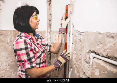 Clever woman repairing her bathroom sink pipe with  positive attitude. Woman using  Bubble Spirit Water Ruler Tool while setting up and checking the t Stock Photo