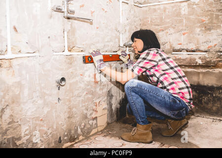 Clever woman repairing her bathroom sink pipe with  positive attitude. Woman using  Bubble Spirit Water Ruler Tool and checking the tubes in the bathr Stock Photo