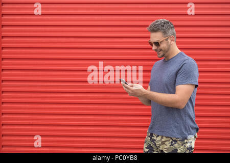 Modern man using smartphone against red background. Space for copy. Stock Photo