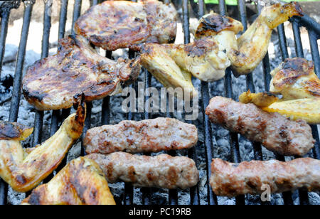 Delicious variety of meat on barbecue grill with char coal. Grilling food on a weber type small cheap BBQ grill at home. Sausages chicken and hot dogs Stock Photo