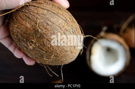 Hand holding a whole coconut on wooden background. .On the right half of the coconut in the bokeh. Stock Photo