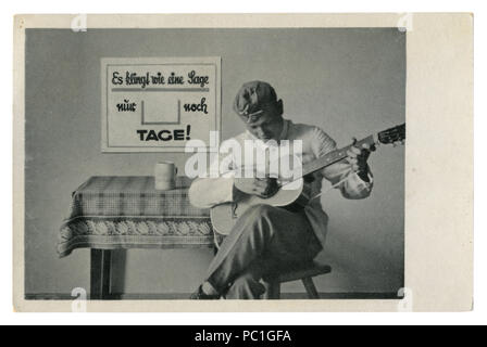 German historical photo postcard: soldier in forage cap plays guitar sitting on a chair. The army's leisure, world war two, Germany, Third Reich Stock Photo