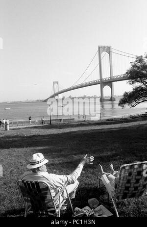 People relaxing in park by Hudson River, New York. Bronx- Whitestone Bridge connecting Bronx to the Queens in New York City. Stock Photo