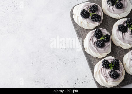 Pavlova dessert cakes with soft lavender cream and fresh blackberries on grey stone cutting board, white textured background Stock Photo