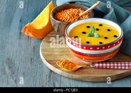 Spicy pumpkin soup with red lentils and turmeric served with mint leaves and drops of balsamic vinegar. Soup ingredients are on wooden rustic backgrop Stock Photo