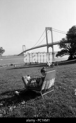 People relaxing in park by Hudson River, New York. Bronx- Whitestone Bridge connecting Bronx to the Queens in New York City. Stock Photo