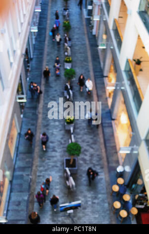 Top view of people walking down the avenue shoppers in a shopping center with restaurants and green plants. Blurry Stock Photo