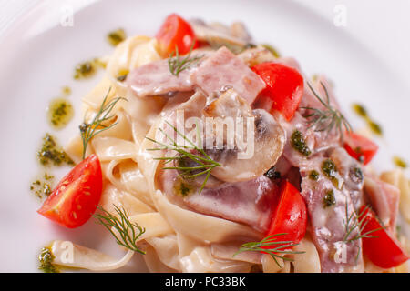 tagliatelle with mushrooms . Italian Pasta on white plate with champignons, ham and tomato Stock Photo