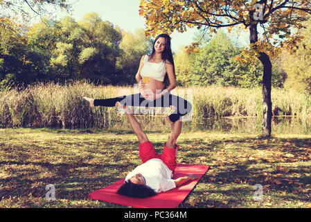 Autumn yoga in the park Man and pregnant woman doing acro yoga. Selevtive focus Stock Photo