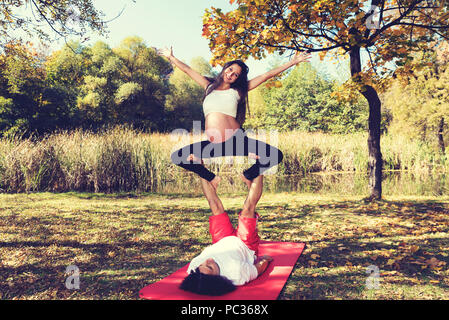 Young couple doing acro yoga. Pregnant woman above his man smiling. Selective focus Stock Photo
