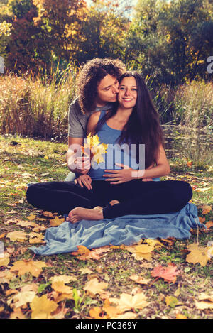 Young man kissing his pregnant  wife in the autumn park. Selective focus Stock Photo