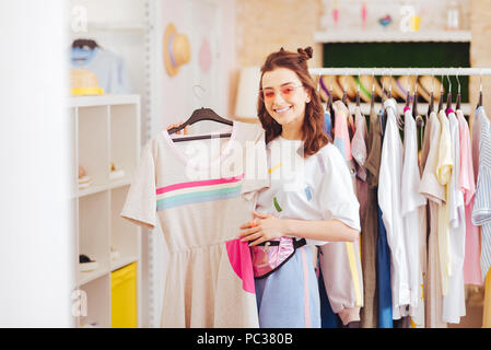 Pink clothes. Beaming good-looking woman being fond of pink clothes buying new dress in favorite shop Stock Photo