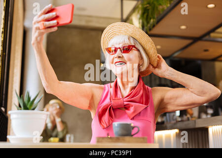 Fashion blogger. Delighted nice woman taking selfies while sitting in the cafeteria Stock Photo