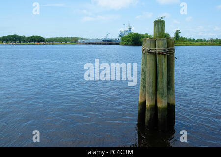 The Cape Fear River Basin with the U.S.S. North Carolina Battleship across the water, wooden pylon wrapped with rope and a plant growing at the top. Stock Photo