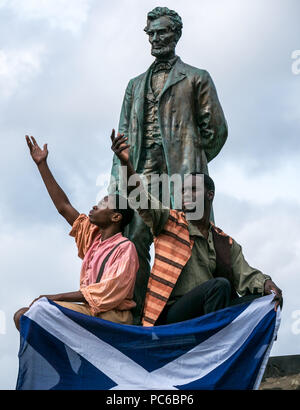 Edinburgh Fringe Festival, Henry Box Brown: Musical Journey photocall, 1st August 2018. Edinburgh, Scotland, UK. The cast at Abraham Lincoln Memorial, Old Calton Burial Ground, which commemorates Scots who fought on with the Union in America. Ben Harney and writer Mehr Mansuri create the musical about a 1850s Virginia slave who ships himself to freedom in a box. Black American actors salute Abraham Lincoln holding Scottish Saltire flag Stock Photo