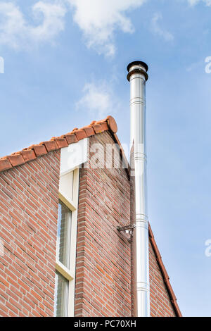 Metal chimney pipe on brick wall of home with blue sky Stock Photo