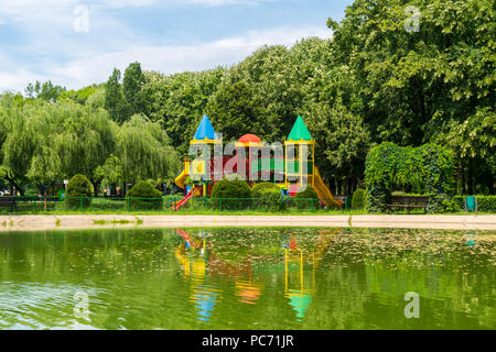 Empty colorful children playground castle with green lush vegetation background and water lake reflection in the foreground situated at Olimpia park i Stock Photo