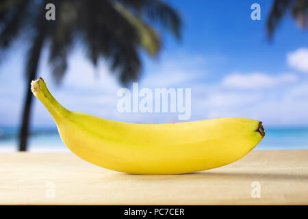One whole fresh yellow banana with palm trees on the beach in background Stock Photo