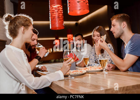 close friends sitting together in pizzeria and hanging out women and men talking eating pizza drinking beer and wine concept of gastronomy cuisine and delicious food pc7fnk