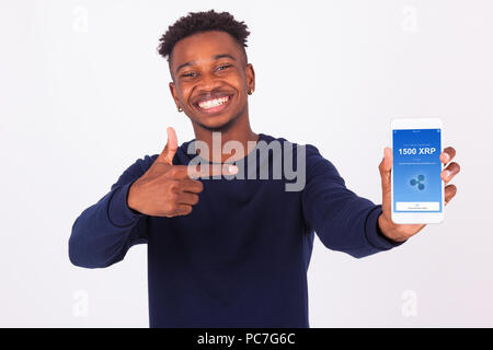 Young African American man pointing his smartphone screen  showing a received crypto currency transaction of ripple xrp received - Black teenager peop Stock Photo
