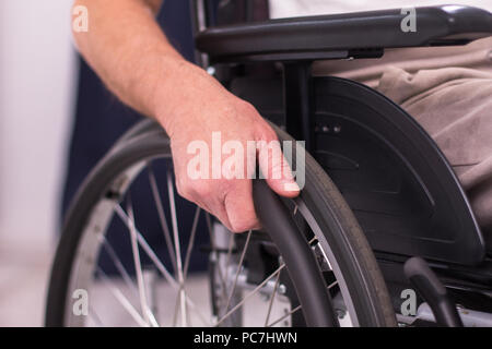 Close up shot of mans hand on wheelchairs wheel. Senior mans hand pushing rubber wheel of wheelchair. Stock Photo