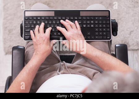 Aged mans hand typing on keyboard. Picture of hands of man who is sitting in wheelchair typing on black computer keyboard taken from above. Stock Photo