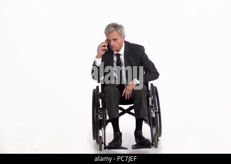 Disabled eldrly man talking on phone while sitting in wheelchair. Handsome aged businessman with grey hair sitting in wheelchair and having conversati Stock Photo