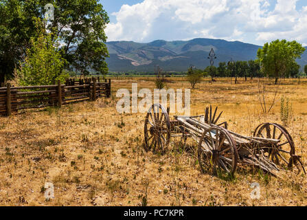 TAOS, NM, USA-8 JULY  18: An ancient, deteriorating wagon with wood spokes and metal rims sits abandoned in a field beside Overland Sheepskin Ranch. Stock Photo