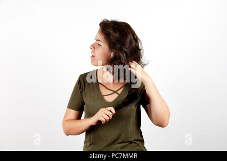 Beautiful young tanned woman in casual dark green shirt with closed eyes and open mouth feeling pain and unpleasant sensations while brushing dark tan Stock Photo