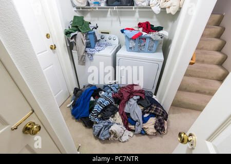 Cluttered messy laundry room with piles of clothes needing to be washed. Stock Photo