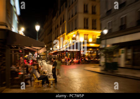 Blurry motion image of people at cafes and bistros at night in Paris. Stock Photo