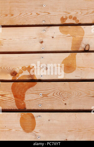 Wet prints of two human feet on brown wooden deck floor. Closeup view. Stock Photo