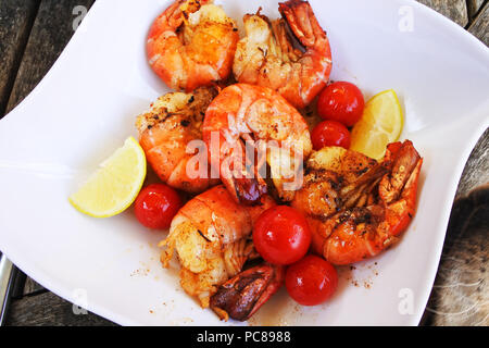 Cooked King Prawns with lemon and tomatoes served on a white plate - John Gollop Stock Photo