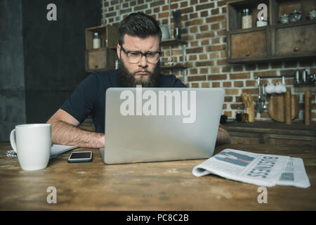 Focused bearded young man using laptop and working at wooden table Stock Photo