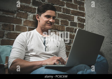 Portrait of man using laptop while leaning to brick wall at workspace Stock Photo